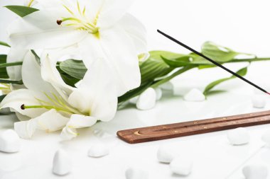 Beyaz arka planda zambakların yanında ahşap tezgahta aroma çubuğu var.