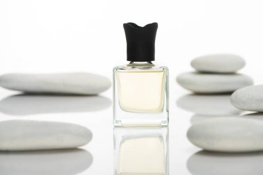 selective focus of home perfume in bottle near spa stones on white background clipart