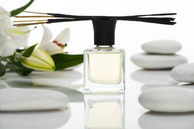 selective focus of aroma sticks and perfume near spa stones and lilies isolated on white clipart