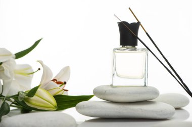Beyaz zambakların yanındaki spa taşlarında aroma çubukları ve parfüm.