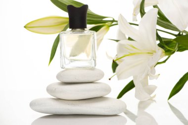 Beyaz arka planda spa taşları ve zambakların yanındaki şişe içinde ev parfümü