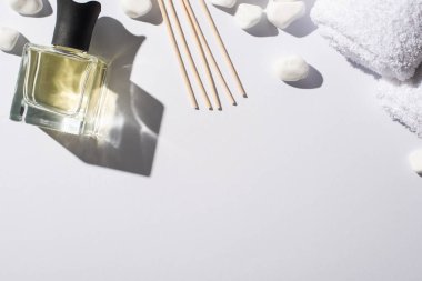 Parfüm şişesinde spa taşlarının yanında ve beyaz arka planda havlu bulunan aroma çubuklarının üst görüntüsü.