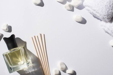 Parfüm şişesinde spa taşlarının yanında ve beyaz arka planda havlu bulunan aroma çubuklarının üst görüntüsü.