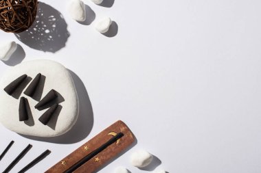 Beyaz zemin üzerinde siyah tütsü konileri, taşlar, aroma çubukları ve dekoratif topun üst görünümü