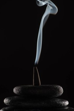 Siyah arkaplanda taşların üzerinde duman olan tütsü külahı yakmak