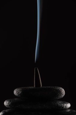 burning incense cone with smoke on stones on black background clipart