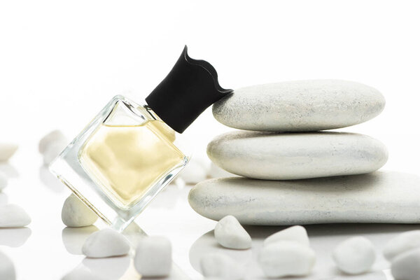 selective focus of home perfume in bottle near spa stones on white background