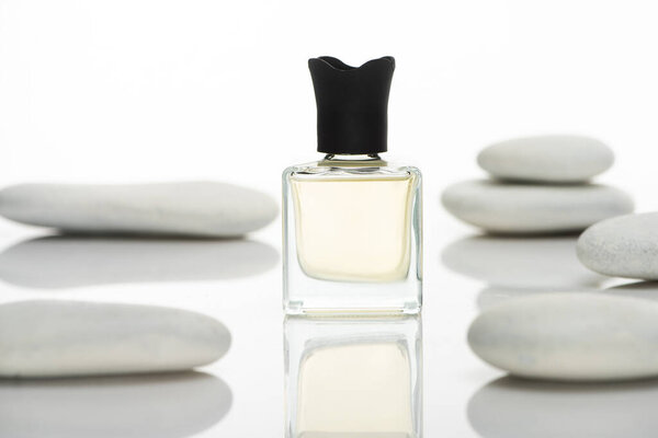selective focus of home perfume in bottle near spa stones on white background