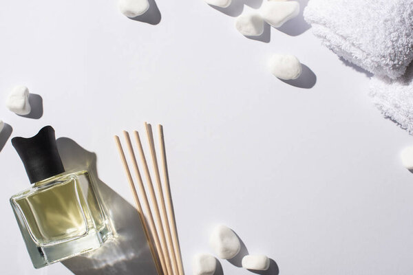 top view of aroma sticks with perfume in bottle near spa stones and towel on white background