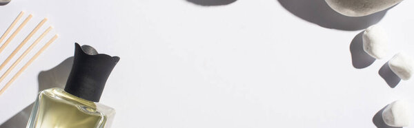 top view of aroma sticks with perfume in bottle near stones on white background, panoramic shot