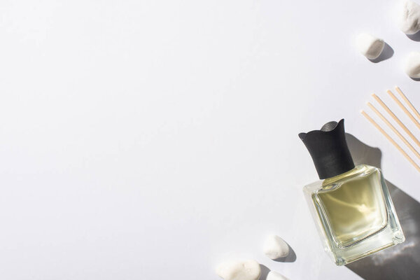 top view of aroma sticks with perfume in bottle near stones on white background