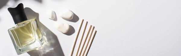 top view of aroma sticks with perfume in bottle near stones on white background, panoramic shot