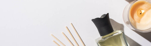top view of aroma sticks with perfume in bottle near candle on white background, panoramic shot