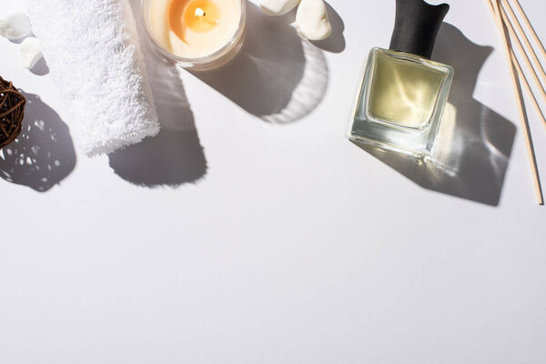 top view of aroma sticks with perfume in bottle near cotton towel, stones and candle on white background