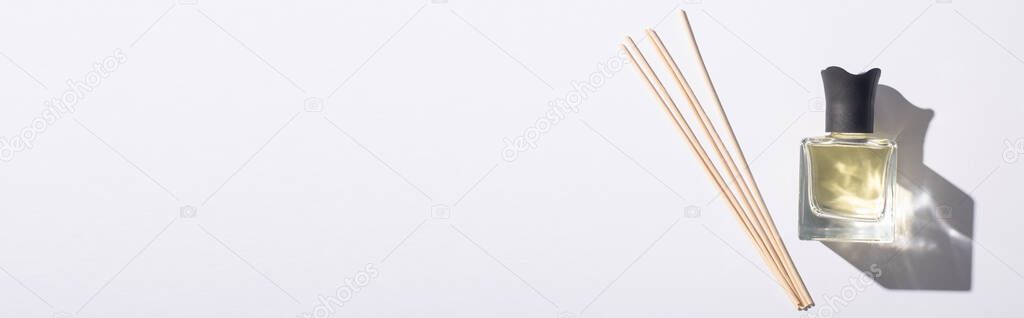 top view of aroma sticks near perfume in bottle on white background, panoramic shot