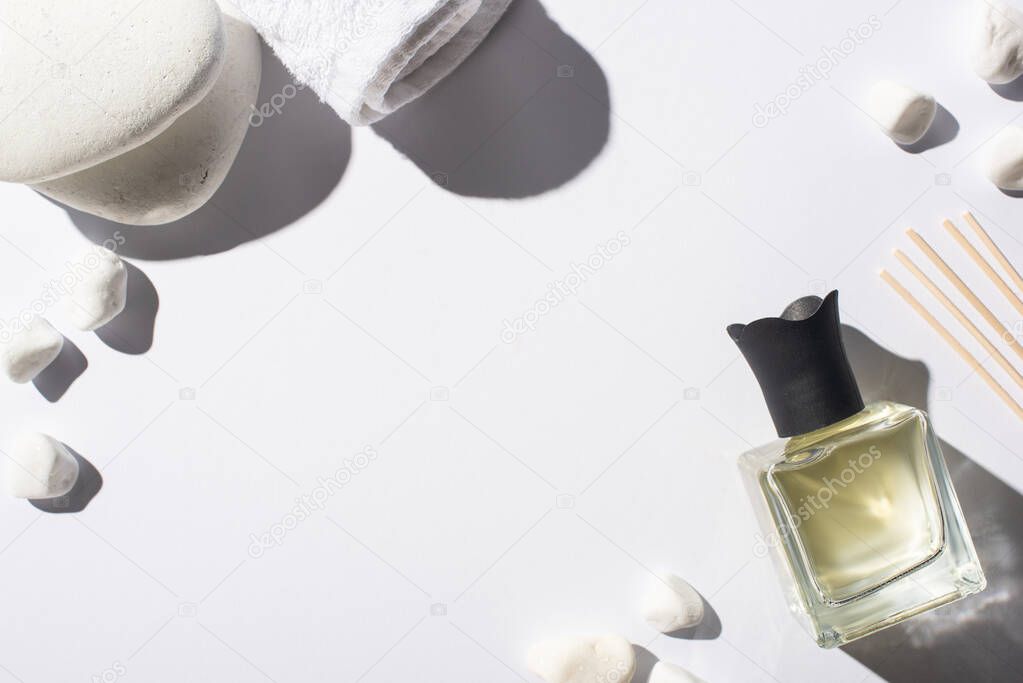 top view of aroma sticks with perfume in bottle near spa stones and towel on white background