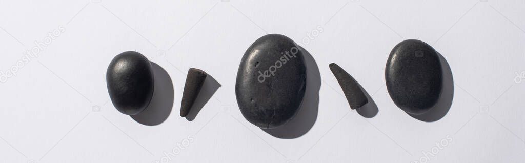 top view of black incense cones and spa stones on white background, panoramic shot