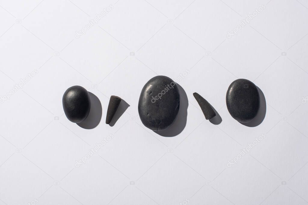 top view of black incense cones and spa stones on white background
