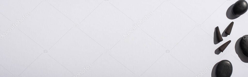 top view of black incense cones and stones on white background, panoramic shot