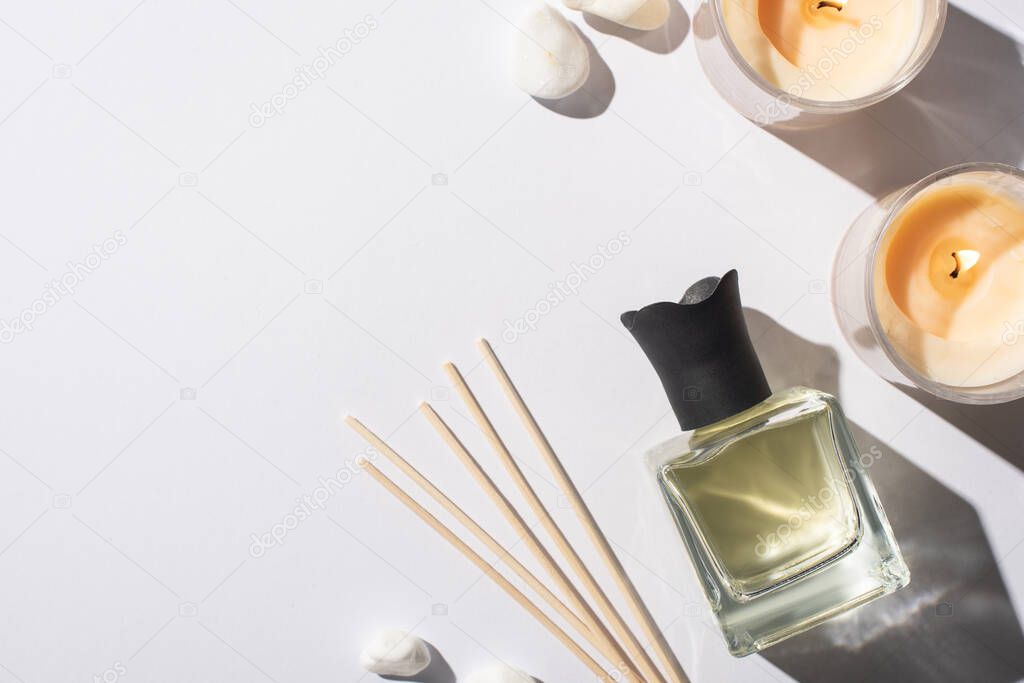 top view of aroma sticks with perfume in bottle near stones and candles on white background