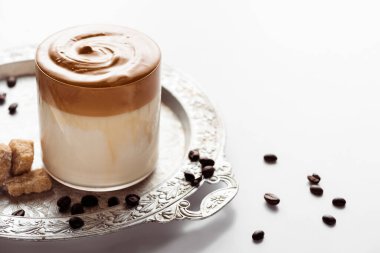 delicious Dalgona coffee in glass near coffee beans, brown sugar on silver platter on white background clipart
