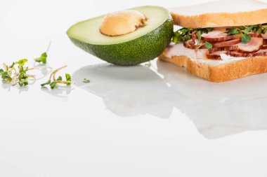 Avokado yakınlarındaki beyaz yüzeyde etli ve lahanalı taze lezzetli sandviç.