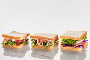 Taze yeşil sandviçler, beyaz mermer yüzeyde avokado ve jamon.