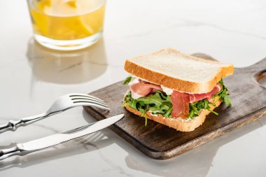 Taze yeşil sandviç roka ve ahşap kesme tahtasında prosciutto beyaz mermer yüzeyde çatal bıçak takımı.