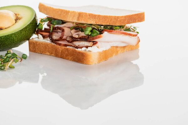 fresh delicious sandwich with meat and sprouts on white surface near avocado