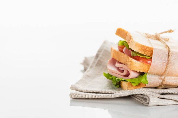 Свежий вкусный сэндвич с нарезанной колбасой и салатом на салфетке на белой поверхности
