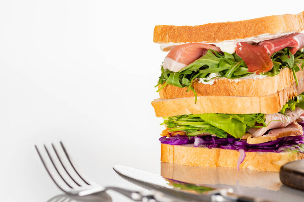 selective focus of fresh sandwiches with meat near cutlery on white surface