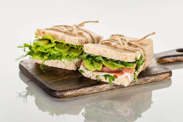 白い表面の木の板にアボカドと肉がのった新鮮な緑のサンドイッチ — ストック写真