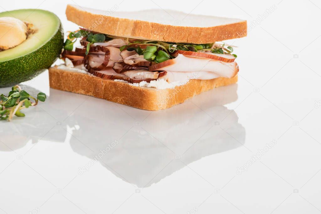fresh delicious sandwich with meat and sprouts on white surface near avocado