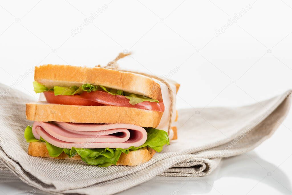 fresh delicious sandwich with sliced sausage and lettuce on napkin on white surface