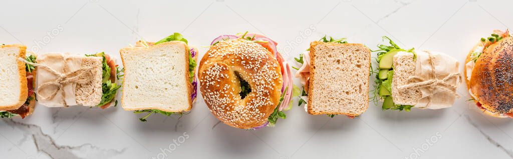 flat lay with fresh sandwiches and bagels on marble white surface, panoramic shot