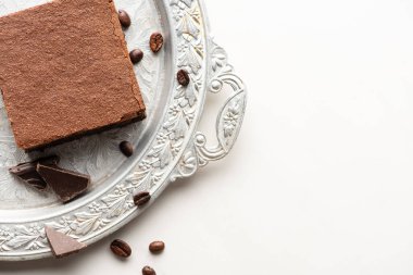 Kahve çekirdekleri ve beyaz arka planda gümüş tepside çikolata ile nefis browni parçasının üst görüntüsü.