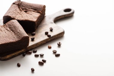 Tahta kesme tahtasındaki lezzetli browni parçalarının seçici odağı beyaz arka planda kahve çekirdekleri.
