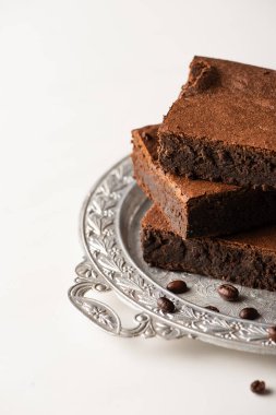 Beyaz arka planda gümüş tepside kahve çekirdekleri ile servis edilen lezzetli browni parçaları.