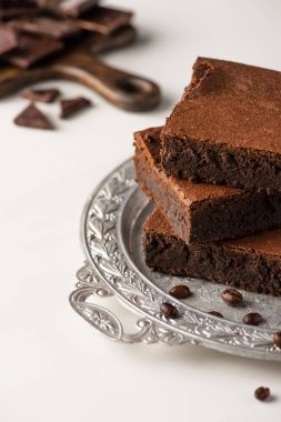Gümüş tepside lezzetli browni parçaları ve beyaz arka planda kahve çekirdekleri.