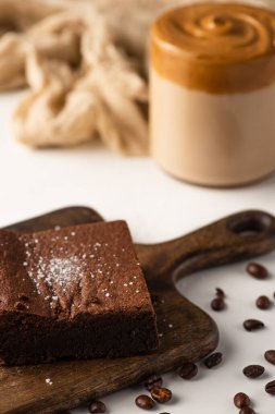 Tahta kesim tahtası ve beyaz arka planda kahve çekirdekleri üzerine nefis browni parçasının seçici odağı.