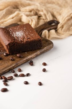 Tahta kesme tahtasında nefis browni parçaları ve beyaz arka planda kumaşın yanında kahve çekirdekleri.