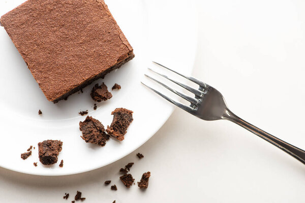 top view of delicious brownie piece on plate with fork on white background