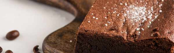 close up view of delicious brownie piece on wooden cutting board with coffee beans on white background, panoramic shot