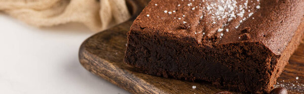 close up view of delicious brownie piece on wooden cutting board on white background, panoramic shot