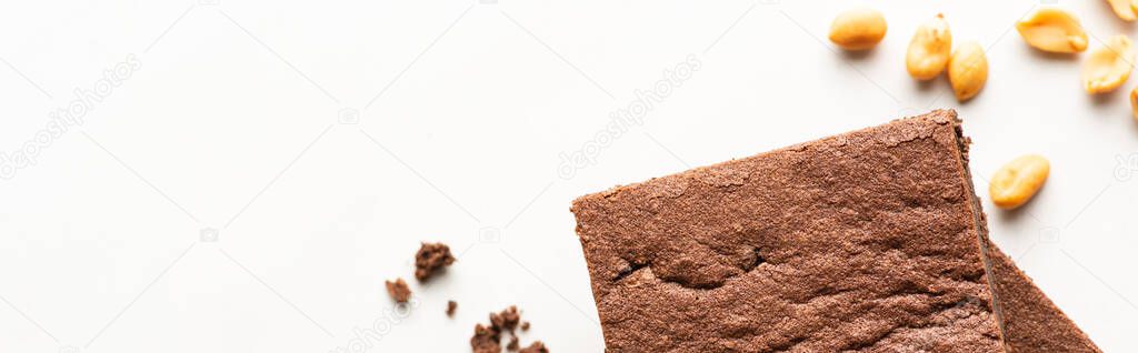 top view of delicious brownie pieces and peanuts on white background, panoramic shot