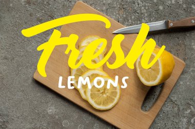 Ağaç kesme tahtasındaki dilimlenmiş limon manzarası gri beton yüzey üzerinde bıçak, taze limon çizimi