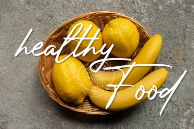 Gri beton yüzey üzerinde sepette renkli muz ve limonların üst görüntüsü, sağlıklı besin örnekleme
