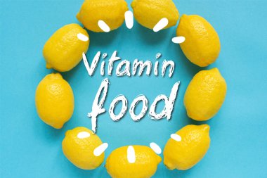 Yuvarlak çerçeveye dizilmiş olgun sarı limonların üst görüntüsü mavi arkaplanda vitamin besin resimleriyle.