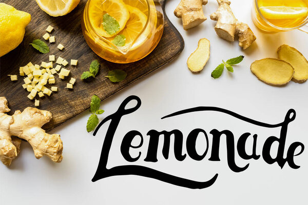 верхний вид горячего чая возле корня имбиря, лимона и мяты на деревянной доске резки на белом фоне, иллюстрация лимонада
