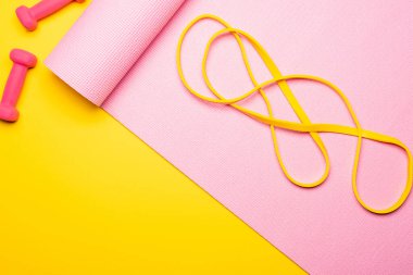 Sarı arka plandaki dambılların yanında pembe fitness minderinde direnç bandının üst görüntüsü